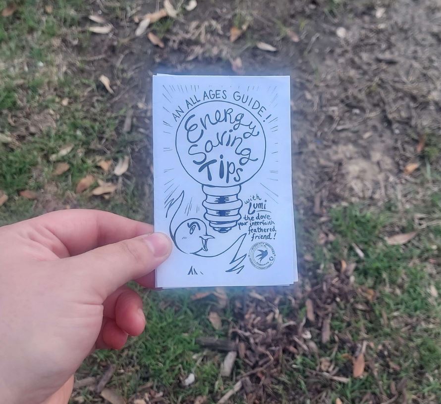 An All Ages Guide! Energy Saving Tips Zine with Lumi the dove your interfaith feathered friend. This is a small 8 page zine being held in my hand above a grassy background.